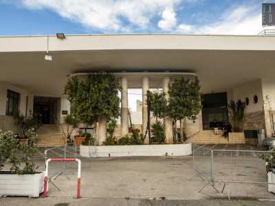 Per farlo ci avviciniamo allo stabile introdotto da una pensilina retta da larghe colonne che lascia spazio alla scalinata di ingresso